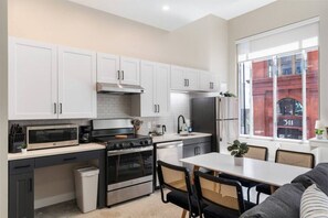 This modern kitchen features a spacious island with cabinetry, sleek white countertops, stainless steel appliances, open shelving, and stylish lighting.