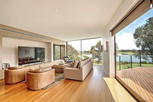 The upstairs living features breathtaking views, plush lounges, leather armchairs,  a Smart TV, and seamless access to the deck for alfresco dining