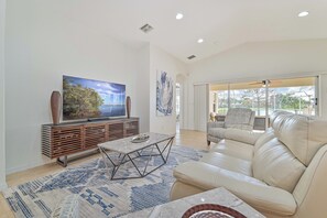 Lake Vista - The living with high vaulted ceilings is equipped with a smart TV, reclining couch and access to the screened in pool area