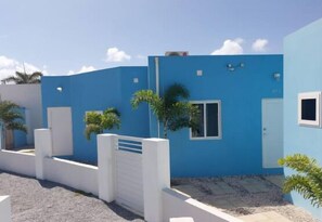 Exterior view of a contemporary building complex. Tropical-style homes with white fences and a paved courtyard.