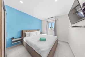 A modern bedroom with a light blue accent wall, a comfortable bed, and a flat-screen TV.