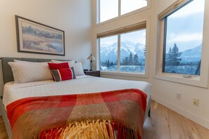 Master bedroom with a queen-sized bed, vaulted ceilings, and expansive windows, offering natural light and picturesque views.