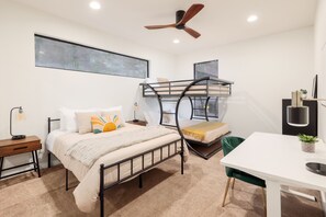 This bedroom has a cozy single bed and a fun bunk bed, perfect for families or groups. It includes a table, chair, cabinets, and a bedside table for each bed, with plenty of natural light for a bright, comfortable space.