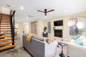 Take in another perspective of our cozy living room, featuring a delightful fireplace and a TV for entertainment. The windows frame beautiful outdoor sceneries, enhancing the room’s relaxing and welcoming vibe.
