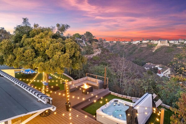 Experience the ultimate outdoor retreat with a cozy fire pit, a relaxing hot tub, a spacious dining area, and breathtaking sunset views beneath a magnificent tree.