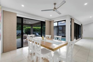 The dining area opens onto the outdoor patio, offering seamless indoor-outdoor living with lush garden and pool views.