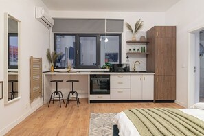 Open-space kitchen equipped with induction stove, electric oven, microwave, mini-fridge, chairs, basic condiments