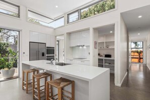 The kitchen features a sleek stone waterfall island bench, quality appliances, and a walk-in pantry with coffee pod machine