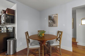 Charming dining nook with a round wooden table, three cushioned chairs, and a potted plant centerpiece. The adjacent modern kitchen includes stainless steel appliances, creating a warm and inviting atmosphere.