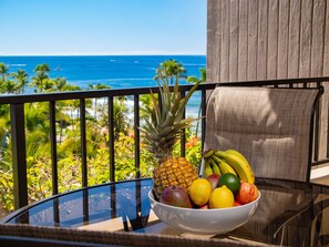 Enjoy breakfast with a stunning ocean view from your private lanai, featuring vibrant tropical fruits and lush greenery.