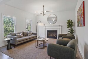 Living room wih fireplace, a coffee table, and large windows for natural light.