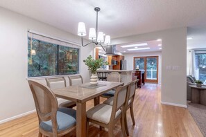 A stylish dining area featuring a sleek six-seat table, elegantly illuminated by a linear chandelier, creating a warm and inviting atmosphere.