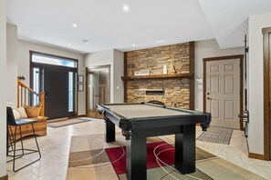 Lower level games room with a pool table, wood-burning fireplace, board games, wet bar & Smart TV.
