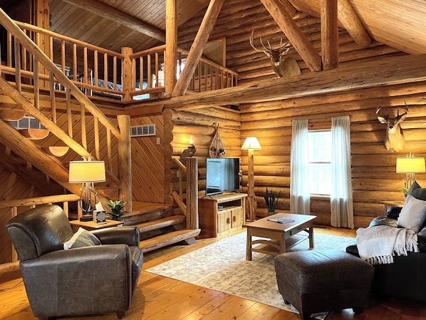Cozy up in the rustic charm of Trillium Lane Cabin’s open-concept living room, featuring warm log interiors, inviting leather seating, nature-inspired decor, and a 50" Roku Smart TV for your entertainment