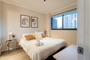 Relax in this stylish bedroom with city views, cozy bedding, and modern decor—your perfect urban retreat.