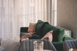 A stylish emerald-green sofa, perfect for unwinding after a day exploring the charms of Poznań's Old Town. Sunlight streaming through the window adds warmth and coziness, creating a unique spot to relax with a view of the city.