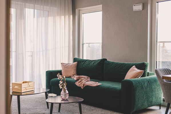 A stylish emerald-green sofa, perfect for unwinding after a day exploring the charms of Poznań's Old Town. Sunlight streaming through the window adds warmth and coziness, creating a unique spot to relax with a view of the city.