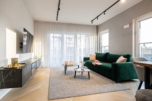 A spacious living room with large windows that flood the space with natural sunlight. A comfortable sofa and TV provide the perfect setting for relaxation after a busy day in Poznań.