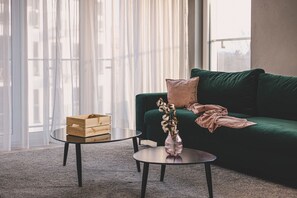 A stylish emerald-green sofa, perfect for unwinding after a day exploring the charms of Poznań's Old Town. Sunlight streaming through the window adds warmth and coziness, creating a unique spot to relax with a view of the city.