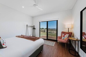 Enjoy the serenity of this peaceful primary bedroom with a king-sized bed featuring a cosy armchair, direct outdoor access, and picturesque rural views.