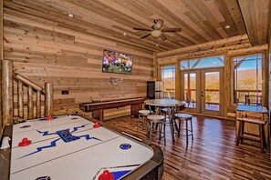Rustic game room: air hockey, shuffleboard, and mountain views.
