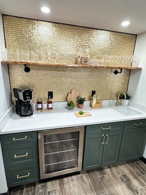 Enjoy your favorite drinks at our stylish wet bar, featuring a wine fridge, elegant glassware, and a stunning gold-tile backdrop – the perfect spot to unwind and celebrate your getaway!
