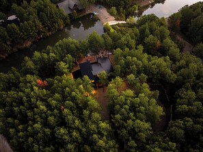 An aerial view of The Cove, beautifully surrounded by a dense forest and a peaceful lake. This secluded getaway offers privacy while still being close to Hochatown and local attractions.