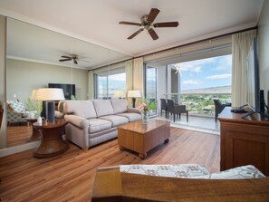 Relax in a bright and airy living room featuring plush seating, ceiling fans, and sliding glass doors opening to a private balcony with scenic views.