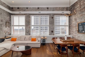 The great room at the end of the hall with 20ft ceilings, offers downtown views, a plush sectional, TV and is open to the ding room and kitchen