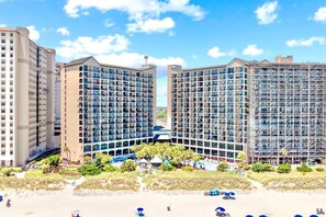 Beachside resort with a sparkling oceanfront pool surrounded by lush palms and sun loungers. Enjoy direct access to pristine sands and coastal views. Relax in this tropical paradise, perfect for soaking up the sun and enjoying seaside bliss.