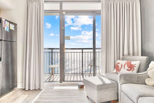 Bright oceanfront beach cove retreat with breathtaking views. Spacious living room features large windows, cozy seating, and coastal decor. Step on the private balcony to enjoy serene sunsets and soothing waves. Perfect for a relaxing seaside escape.