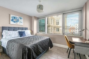 Stylish and serene bedroom with a comfy bed, large windows, and a dedicated workspace—perfect for work or rest.