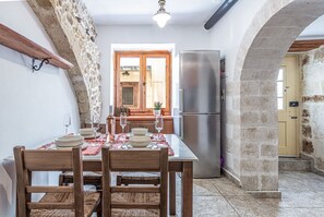 The kitchen of Casa Eleni features a fully equipped cooking space, a refrigerator, and a dining table with four seats, offering both functionality and comfort.