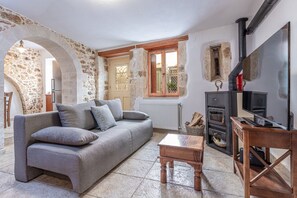 The living room of Casa Eleni includes a cozy sofa, a wood stove for warmth, a smart TV for entertainment, and a nearby WC for convenience.