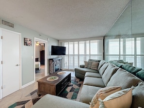 Spacious living area featuring a plush sectional sofa, flat-screen TV, mirrored accent wall, and natural light for a comfortable and stylish retreat.