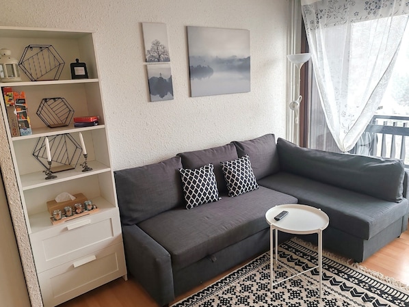 Relax in this stylish living room featuring a comfortable sectional sofa that easily converts into a sofa bed, a chic bookshelf with decorative accents, and large windows that flood the space with natural light.