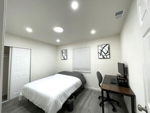 This modern bedroom features a cozy queen bed and a dedicated work desk.