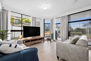 Bright and spacious living room with modern furnishings and large windows, offering a cosy retreat with views of the greenery and natural light.
