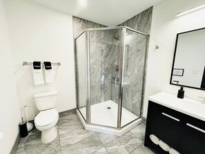  A pristine bathroom featuring a walk-in shower with elegant gray tiles, fresh towels, and modern amenities.