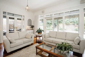 A spacious lounge area featuring a comfortable sofa, a flat-screen TV, and abundant natural light, creating a bright and inviting atmosphere. Perfect for relaxing or enjoying entertainment.