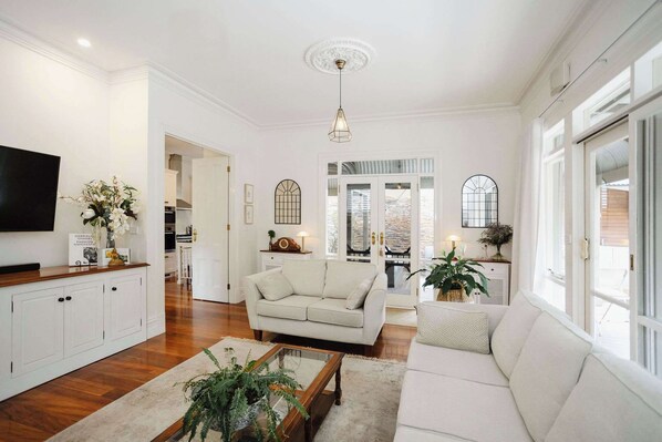A spacious lounge area featuring a comfortable sofa, a flat-screen TV, and abundant natural light, creating a bright and inviting atmosphere. Perfect for relaxing or enjoying entertainment.