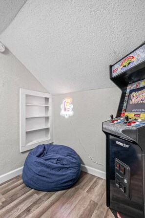 Fun-filled nook featuring a classic arcade machine, vibrant arcade sign, and a comfy bean bag chair—the perfect spot for some downtime!