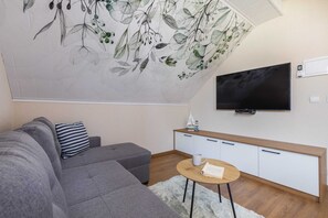 A compact living room area with a modern TV, a gray sofa, and decorative wallpaper.
