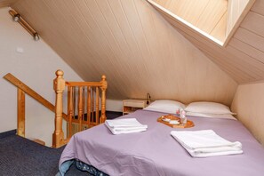A loft-style bedroom with a comfortable bed, soft lighting, and a charming wooden staircase.
