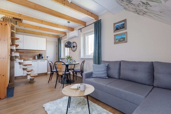 A cozy living room with a gray sofa, wooden beams, and a bright, inviting atmosphere.
