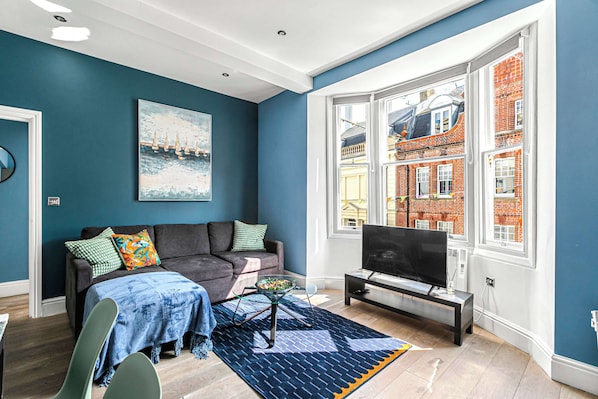 Bright and modern living room with a cozy sofa, smart TV, and large bay window offering plenty of natural light and charming street views