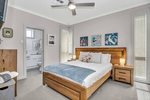 Located downstairs, the primary suite is a tranquil retreat with a queen bed, ensuite bathroom, and soothing artwork. Filled with natural light and enhanced by a ceiling fan, it’s the perfect space to relax and recharge in comfort.