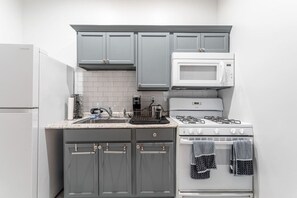 Compact Kitchen Setup Includes a full-size fridge, gas stove, microwave, Keurig coffee maker, sink, dish rack, and storage—great for simple meal prep.