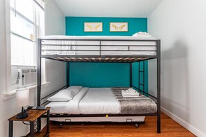 Bright Family Room: Sunny bedroom with Twin-over-Twin Bunk, pull-out Trundle, and full-size Crib—ideal for families. Includes a mini fridge, nightstand, wall-mounted TV, and a convenient luggage stand.