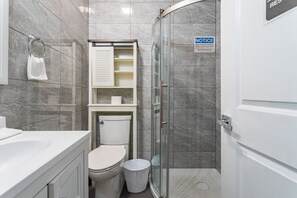 Modern bathroom with sleek tile walls, a glass-enclosed shower, vanity with ample storage, and an over-the-toilet cabinet for added convenience.